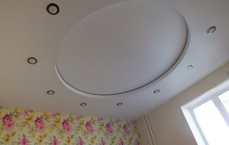 Дворівнева біла матова стеля зі стильним підсвічуванням та вбудованими світильниками створює у спальні атмосферу легкості та затишку. Центральний другий рівень у формі круга додає інтер’єру витонченості та гармонійно акцентує увагу, надаючи простору м'якої об’ємності. М’яке підсвічування підкреслює плавні лінії та створює ідеальні умови для відпочинку. Вишукане рішення для сучасного та стильного інтер’єру спальні!