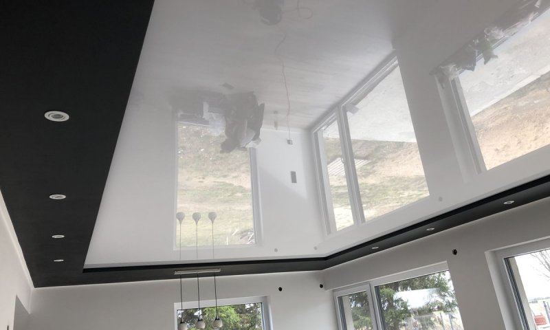 Дворівнева стеля на кухні – ідеальне поєднання елегантності та сучасного стилю. Глянцева біла основа з підсвіткою візуально розширює простір, додаючи йому легкості та сяйва. Контур із матового чорного покриття створює виразний контраст, а вбудовані білі світильники разом із стильними підвісними лампами забезпечують продумане освітлення. Це рішення не тільки додає кухні естетики, а й підкреслює сучасний дизайн із нотками мінімалізму та розкоші.