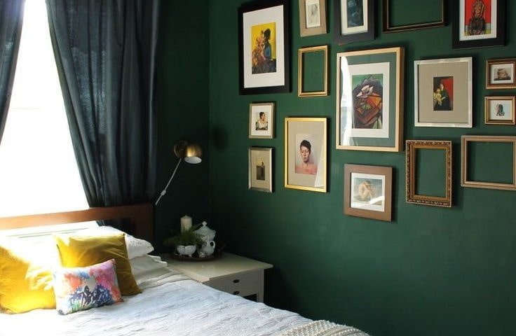 Матова натяжна стеля у глибокому зеленому відтінку створює атмосферу затишку та гармонії у спальні. Темні штори та акцентна стіна з картинами додають простору характеру, а сучасна люстра з латунними елементами завершує стильний образ інтер’єру.